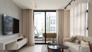 Un salon moderne avec un téléviseur à écran plat, un canapé, une table basse et un balcon agrémenté d’un fauteuil en osier.