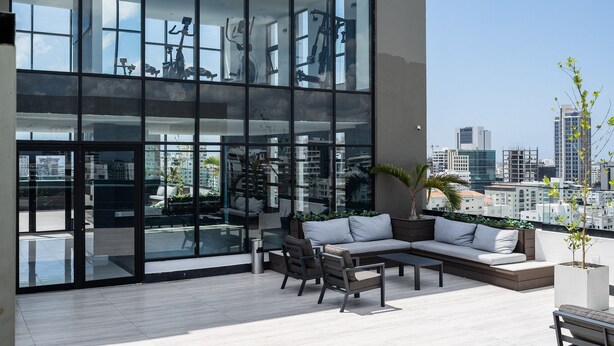 Un espace extérieur moderne, aménagé avec un canapé et des fauteuils, de grandes fenêtres et une vue sur la ville.