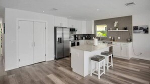 Una cocina moderna con armarios blancos, electrodomésticos de acero inoxidable y una isla central con taburetes de bar.