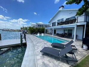 Un espace piscine avec des chaises longues, un quai et un bâtiment doté d’un balcon donnant sur l’eau.