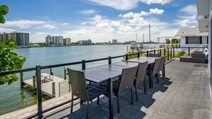 Un patio frente al agua con una mesa y sillas, un muelle y vistas al agua y edificios a lo lejos.
