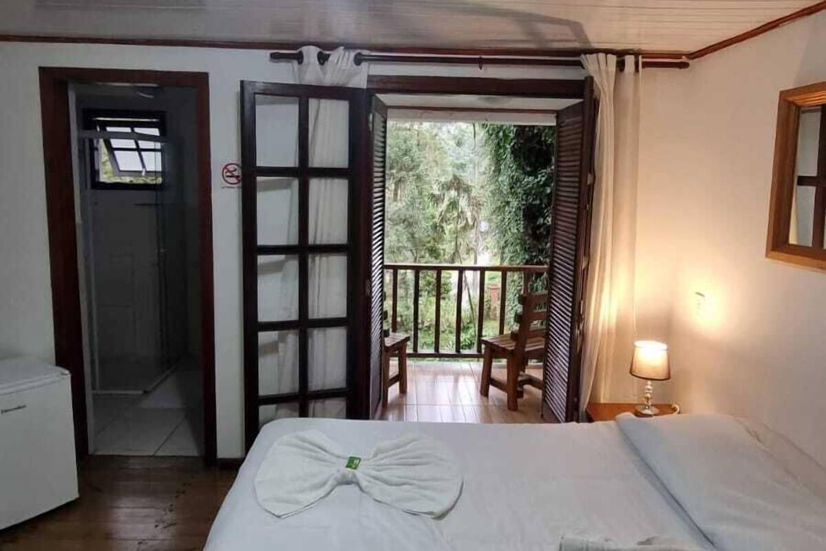 Een kamer met een bed, een klein tafeltje, een stoel en een balkon met uitzicht op groen.