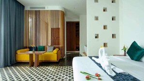 A hotel room with a bed, a wooden partition, a yellow sofa, a small table, and a patterned floor.