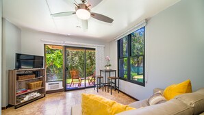 A living room with a sofa, a TV, a bookshelf, and a dining area with chairs and a table. - Kihei Akahi Garden View Studio (Kihei)