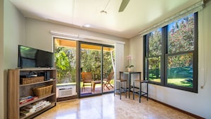 A spacious living area with a television, bookshelf, and a sliding glass door leading to an outdoor patio. - Kihei Akahi Garden View Studio (Kihei)