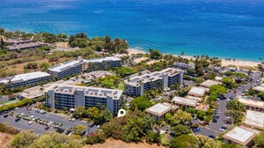 An aerial view of a coastal area with buildings, parking, and a beach. - Kihei Akahi Garden View Studio (Kihei)