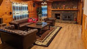 A cozy log cabin interior with a leather sofa, a wooden coffee table, and a stone fireplace.