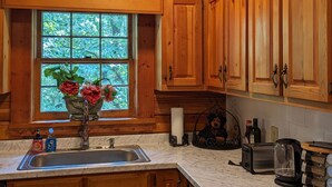 A kitchen with wooden cabinets, a marble countertop, a window with a view of greenery, a vase with flowers, and a teddy bear on the counter.