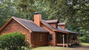 A log cabin with a porch and chimney, surrounded by trees.