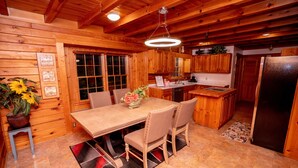 A wooden cabin interior with a dining table, chairs, a kitchen area, and a refrigerator.