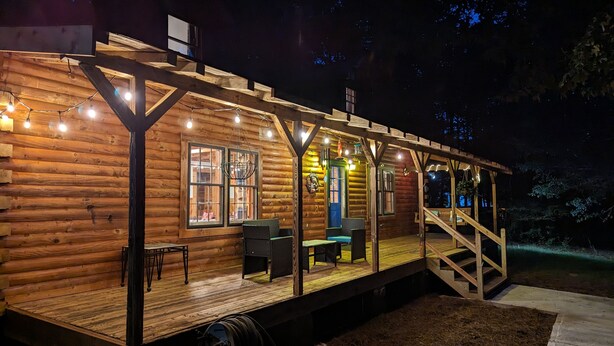 A wooden cabin with a deck, outdoor seating, and string lights.