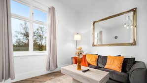 Ett modernt vardagsrum med en soffa, ett soffbord, en vas med blommor, en lampa och en stor spegel på väggen.