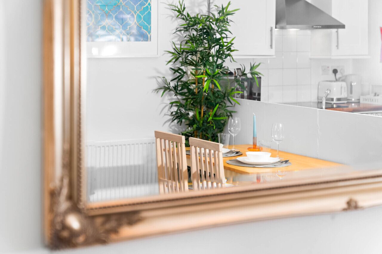 A dining area with a table set for two, a potted plant, and a modern kitchen in the background.