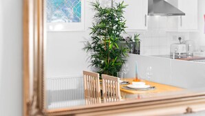 En matplats med ett bord dukat för två personer, en krukväxt och ett modernt kök i bakgrunden.