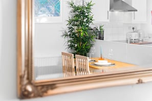 A dining area with a table set for two, a potted plant, and a modern kitchen in the background. - Luxury Apartment - Wolverhampton (Wolverhampton)