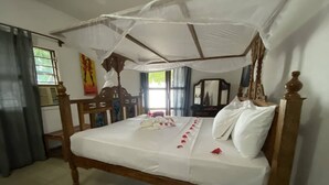 A wooden bed with a canopy, a bedside table, and a mirror. - Menai Bay Beach Bungalows (Unguja Ukuu)