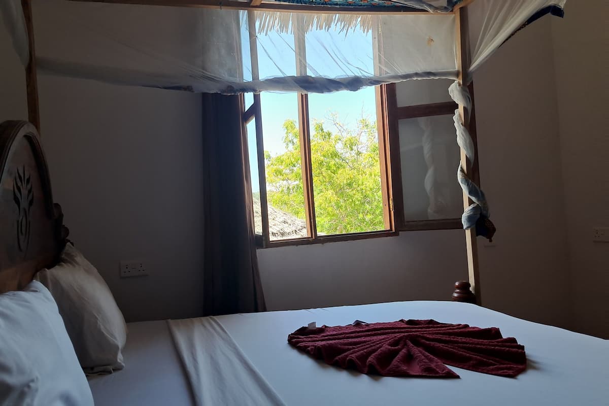 A room with a bed, a window with curtains, and a view of greenery outside.