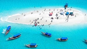 Vista aérea de una isla tropical con aguas turquesas cristalinas, numerosos barcos y gente en la playa.