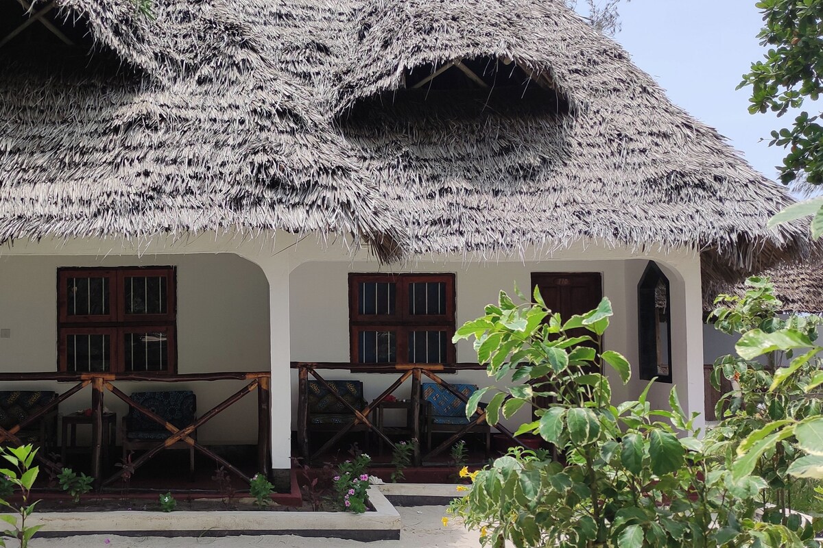 Una casa tradicional con techo de paja y un porche, muebles de madera y el número 703 en la puerta.