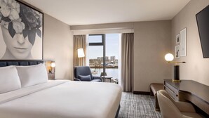 A hotel room with a large bed, a desk, a chair, a lamp, a picture on the wall, and a view of the city through the window. - Radisson Blu Vancouver Airport Hotel & Marina (Richmond)