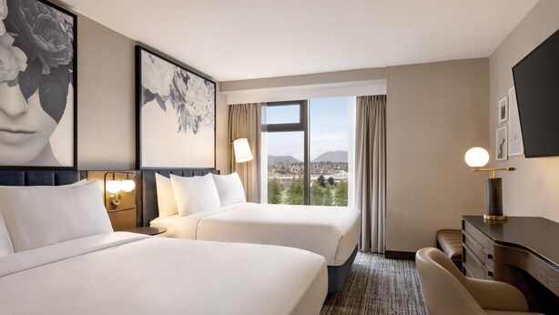 A hotel room with two beds, a desk, a chair, and a large window offering a city view. - Radisson Blu Vancouver Airport Hotel & Marina (Richmond)
