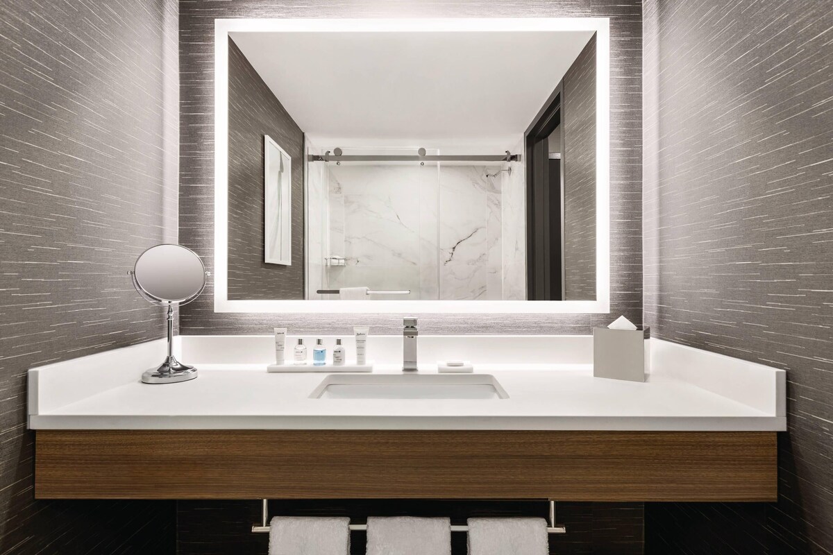 A modern bathroom with a large mirror, white sink, and marble backsplash.