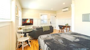 A cozy room with a bed, a sofa, a dining table, and a TV displaying a fireplace.