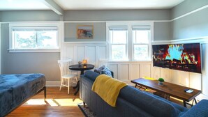 A cozy living room with a sofa, a small table, a TV, and a window with a painting above it. - Desirable Studio Park Views W/D (San Diego)