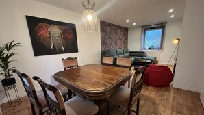 Uma área de refeições com uma mesa e cadeiras de madeira, um sofá verde, um pufe vermelho e um quadro grande de um elefante na parede.