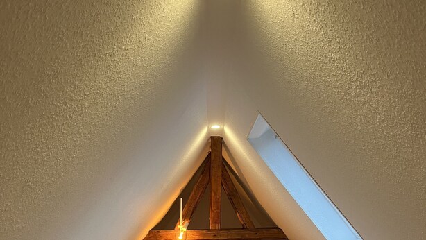 Um quarto de sótão aconchegante com teto inclinado, um claraboia, uma cama com almofadas e uma mesinha.