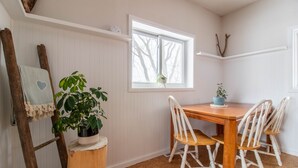 A dining area with a wooden table and white chairs, a potted plant, and a ladder against the wall.