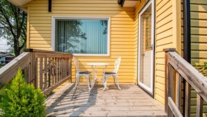 A wooden deck with a table and two chairs, a sliding glass door, and a window with blinds.