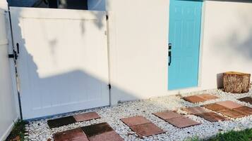 A white building with a blue door, a gated entrance, and a gravel pathway leading to the door.