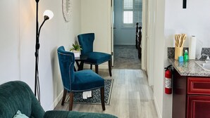 Ein Wohnzimmer mit einem dunkelgrünen Sofa, einem blauen Sessel, einer Stehlampe und einem Essbereich mit Tisch und Stühlen.