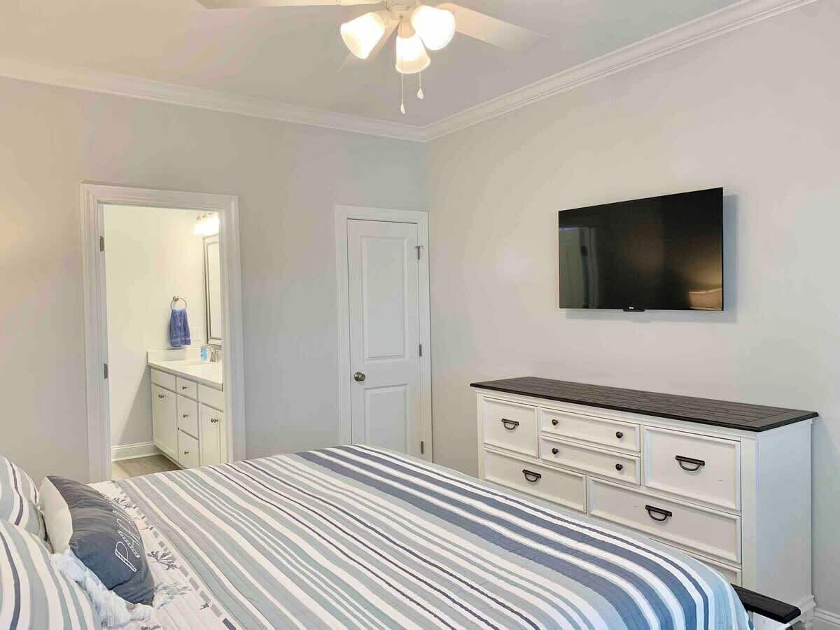 Un dormitorio con cama, cómoda, televisor y puerta que da a un baño.