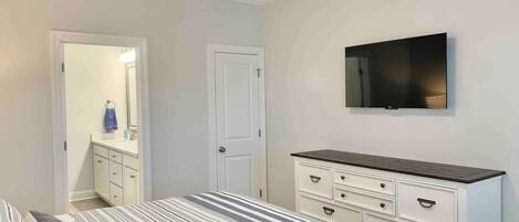 Un dormitorio con cama, cómoda, televisor y puerta que da a un baño.