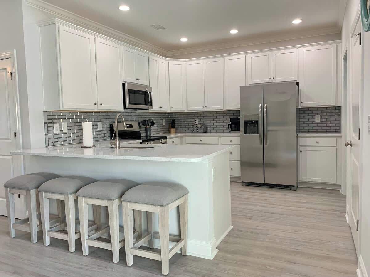 A modern kitchen with white cabinets, a stainless steel refrigerator, a microwave, and a central island with bar stools.