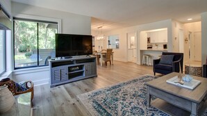 Uma sala de estar ampla com uma televisão de tela plana grande, um espaço de refeições e uma cozinha.