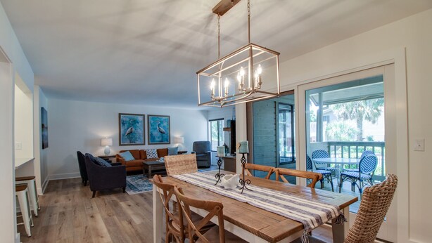 Uma sala de jantar espaçosa com mesa e cadeiras de madeira, luminária pendente e vista para o exterior.