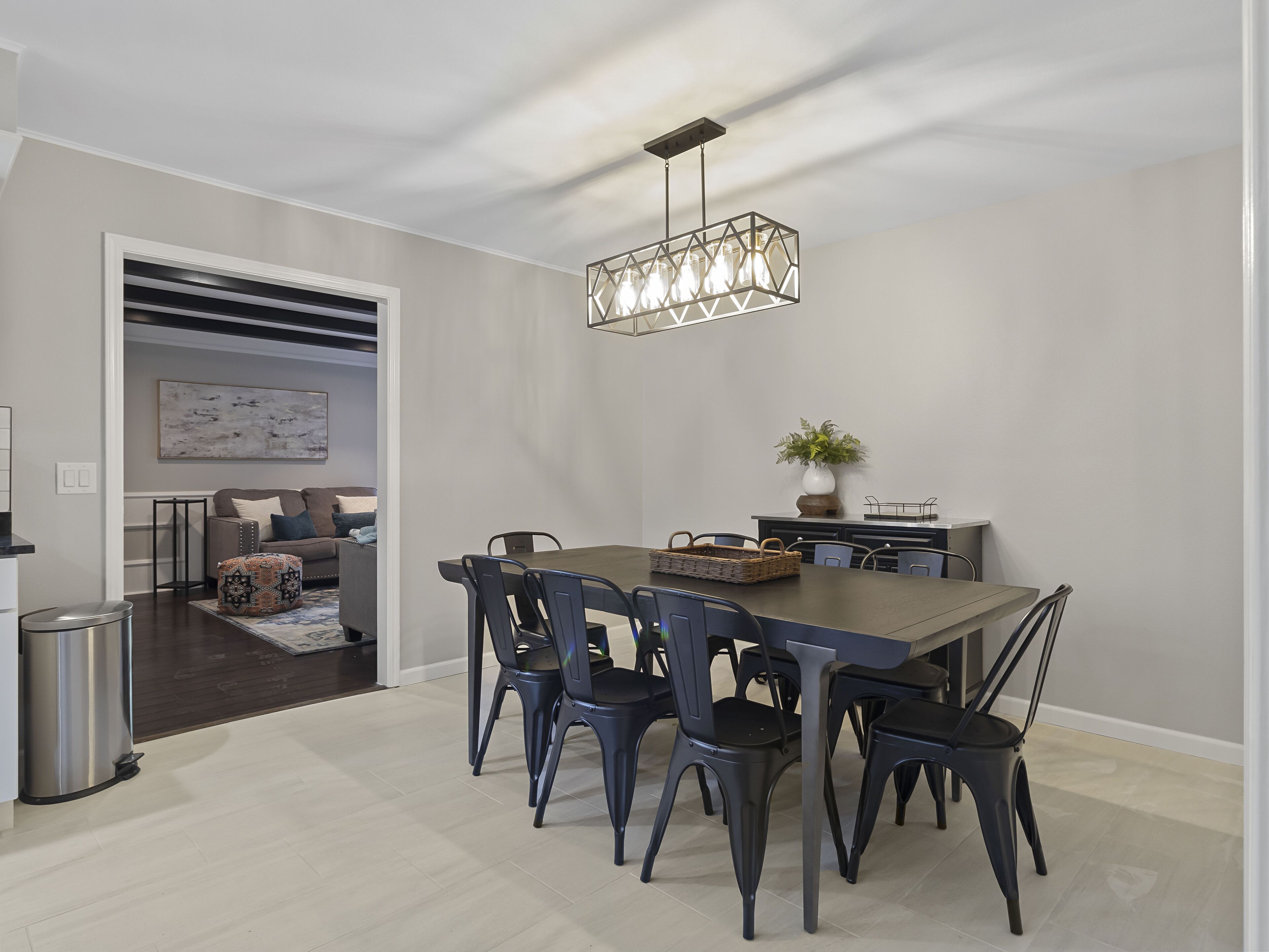 A modern dining area with a dark wooden table and matching chairs, a hanging light fixture, and a potted plant on the side.