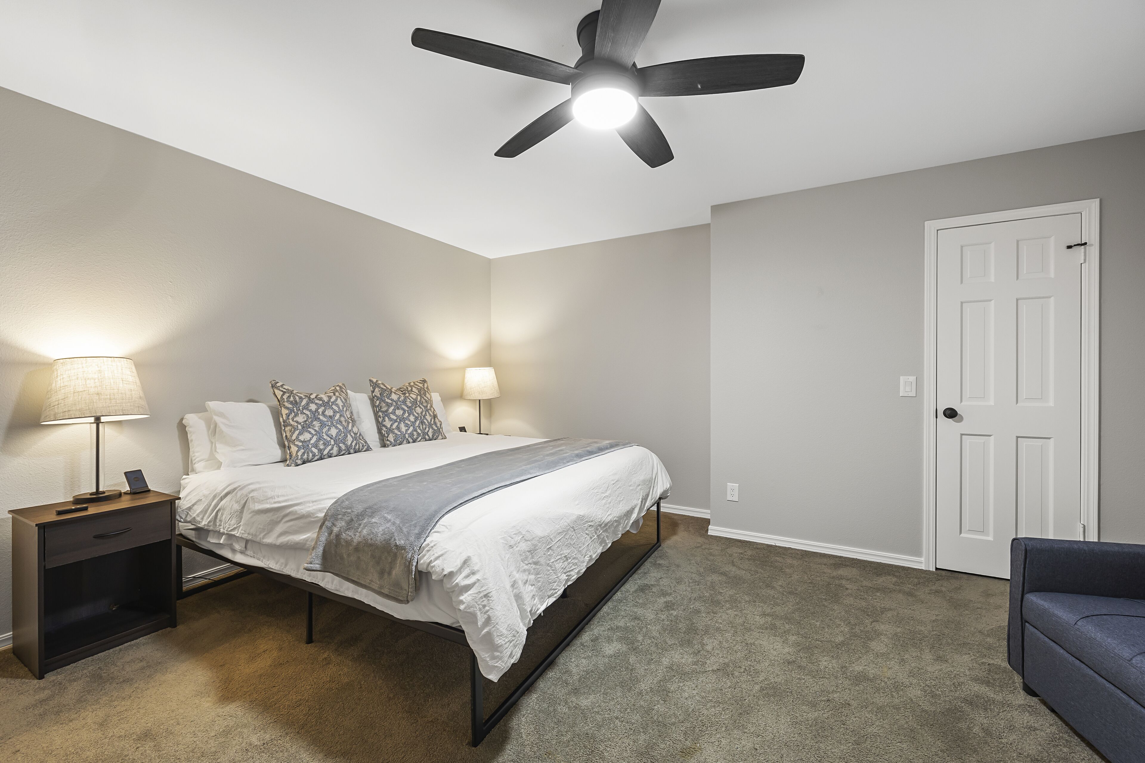 A bedroom with a bed, bedside tables, a ceiling fan, a door, and a chair.