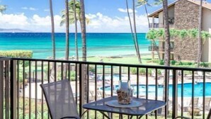 Un balcon avec vue sur l’océan et les palmiers, une table avec des chaises et un espace piscine.