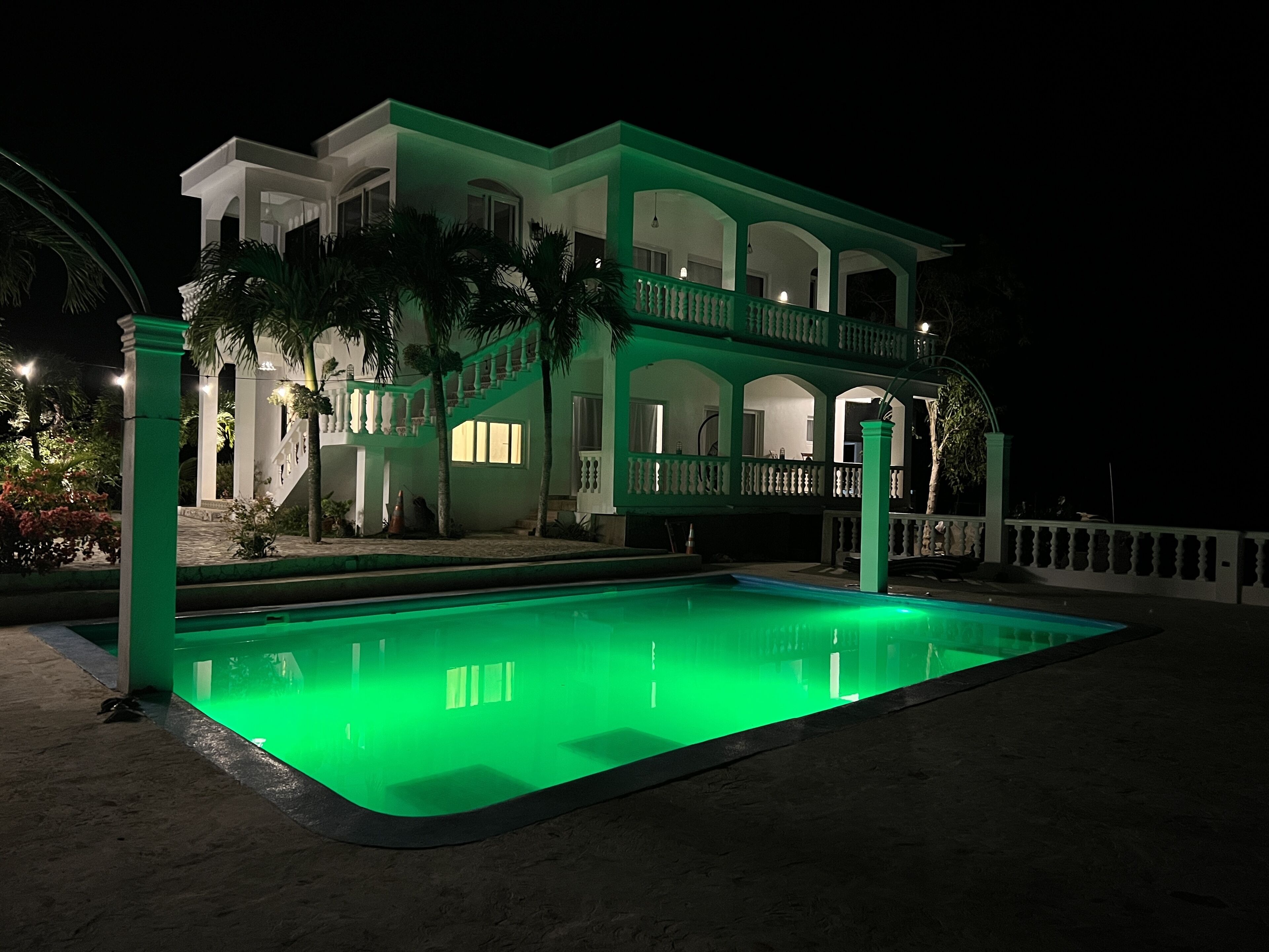 A two-story house with a pool, surrounded by a fence and palm trees.