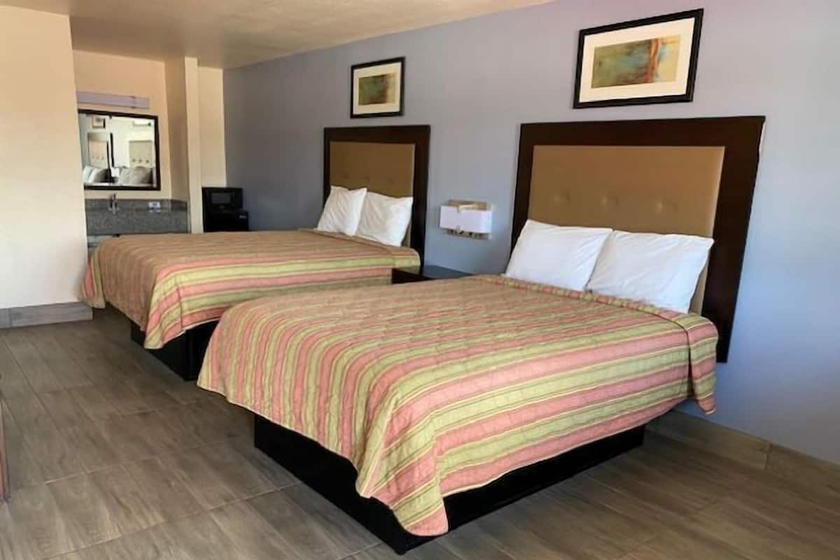 A hotel room with two beds, each with a striped bedspread, a headboard, and a bedside table.