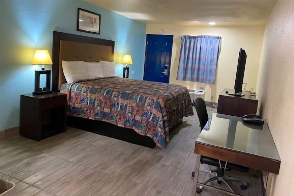 A hotel room with a bed, a desk, a chair, a TV, and a lamp.