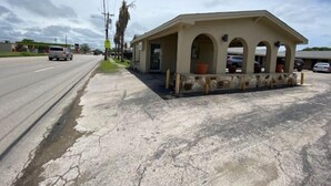 A small building with a covered porch and a stone base, located beside a road with vehicles. - Texas Inn (Seguin)