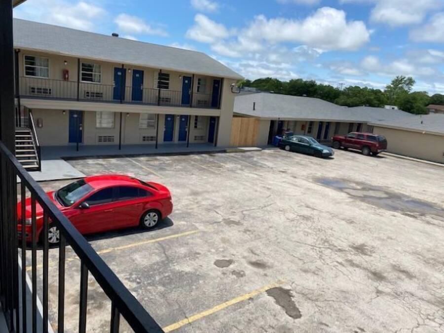 A motel with a parking lot, a red car parked in the foreground, and a building with multiple doors and windows.