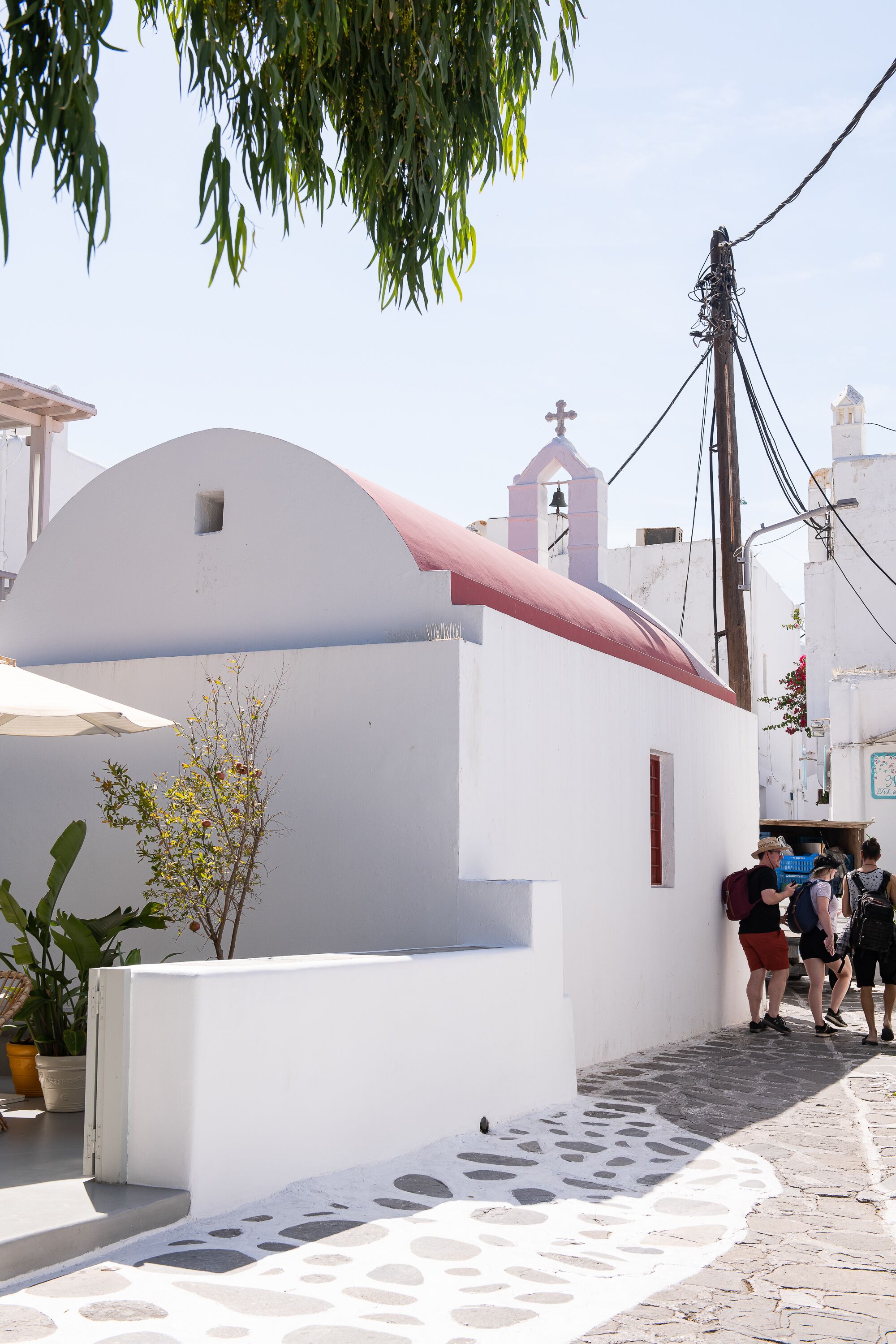 A white building with a red roof, a bell tower, and a stone-paved street.