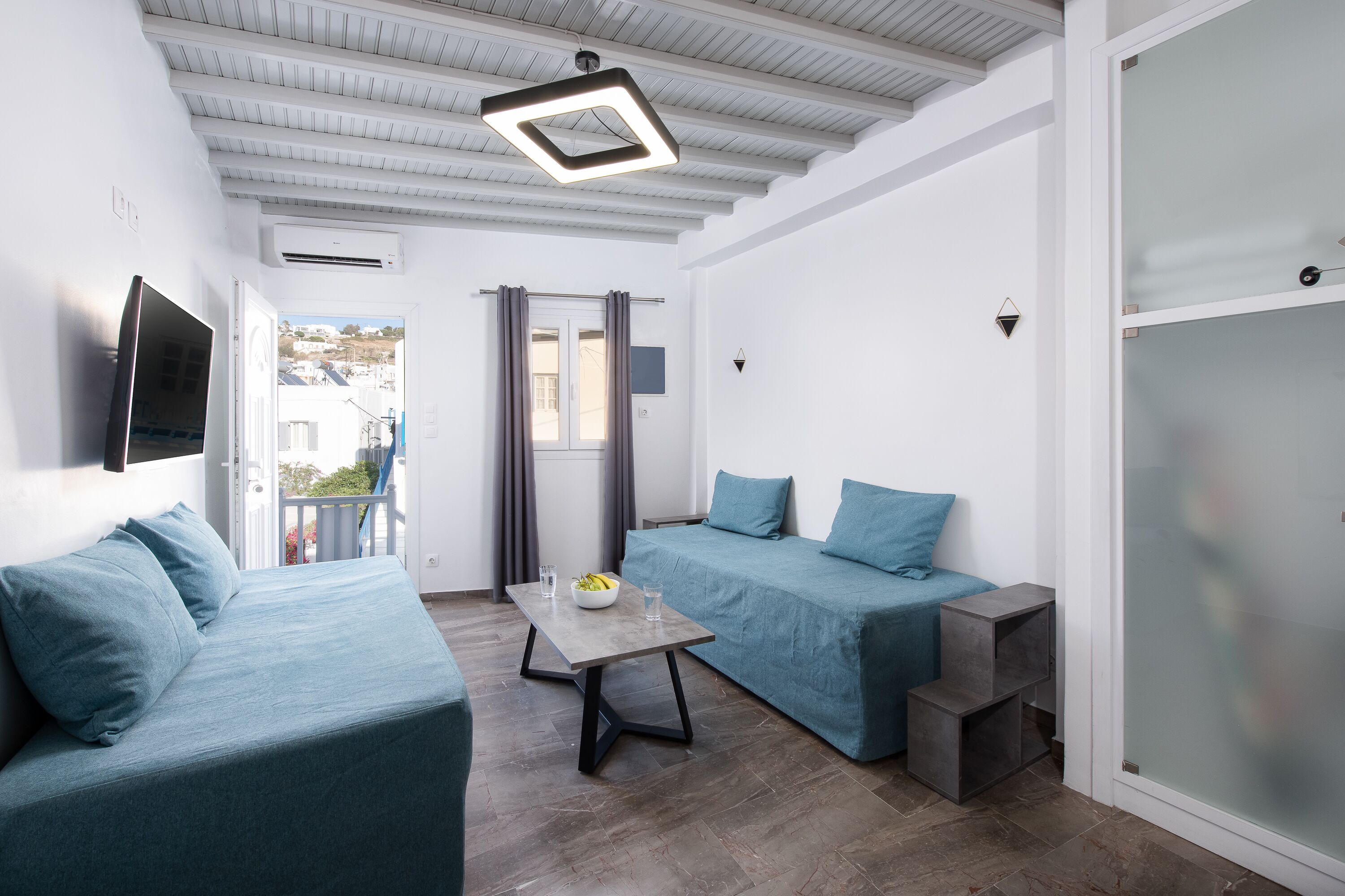 Una sala de estar moderna con dos sofás azules, una mesita con un cuenco y vasos, y una lámpara en el techo.