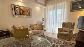 A living room with a glass coffee table, a sofa, a chair, and a TV. - LAKEHOUSE ENJOY (Pallanza)
